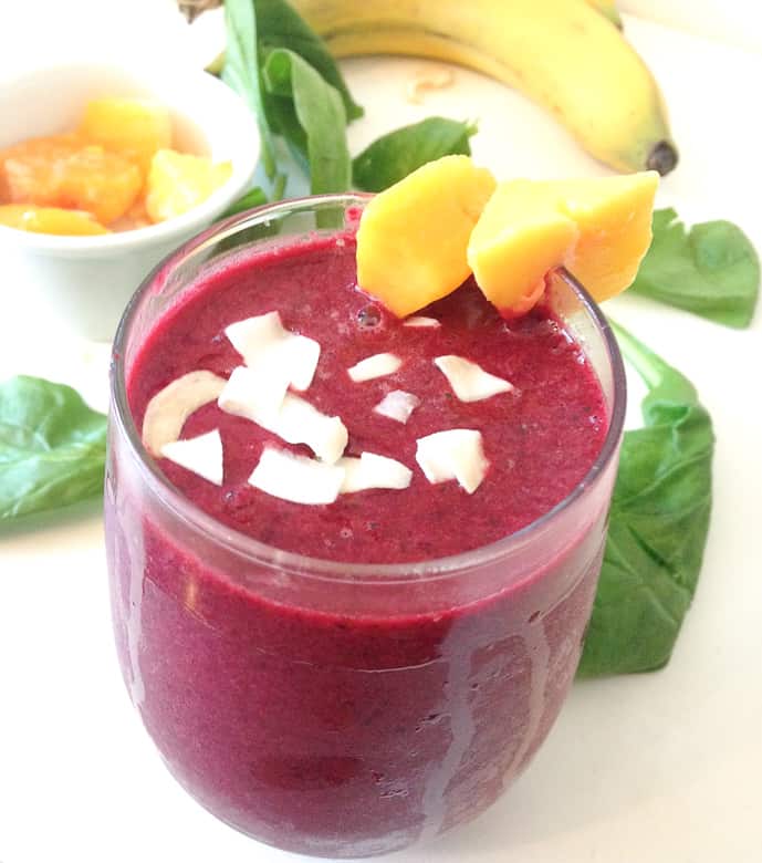 beet spinach smoothie topped with coconut flakes and mango slices