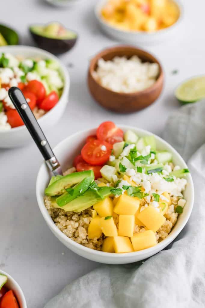 Bowl of summer quinoa salad with sliced mangos, lime and tomatoes with a fork