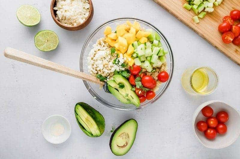Clear bowl with mango and quinoa salad topped with diced vegetables