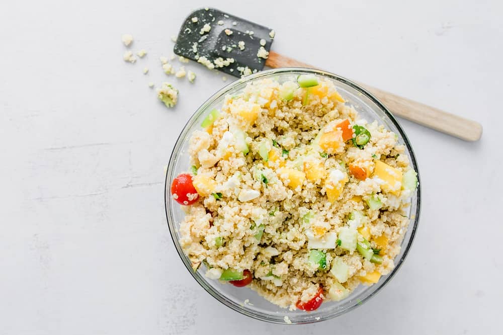 Clear bowl of mixed mango quinoa salad on white counter