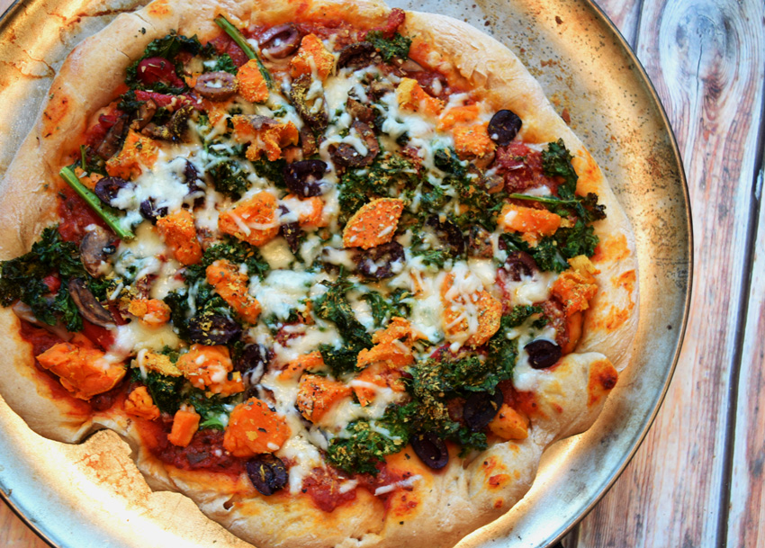 Overhead final shot of kale pizza with sweet potatoes olives and cheese