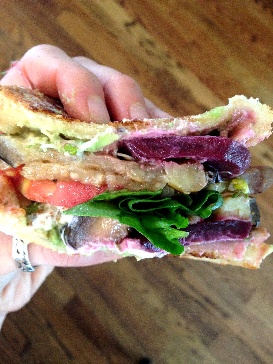 Holding up eggplant goat cheese avocado sandwich with other veggies