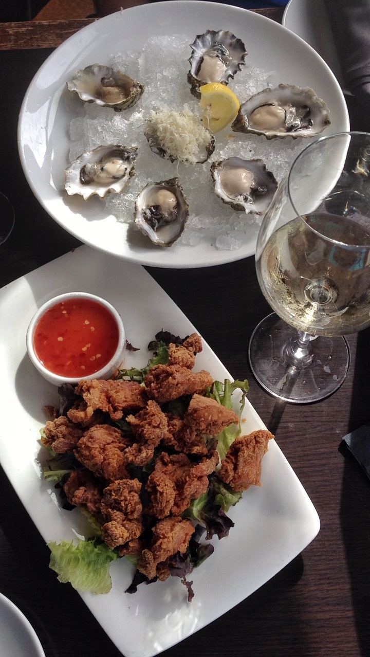 Oysters and calamari on white plates with glass of wine for happy hour