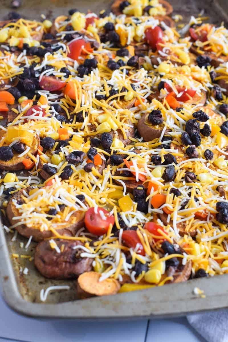 cut sweet potatoes on sheet pan topped with beans, tomatoes and shredded cheese