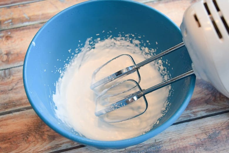 Whipping canned coconut in a blue bowl with hand mixers
