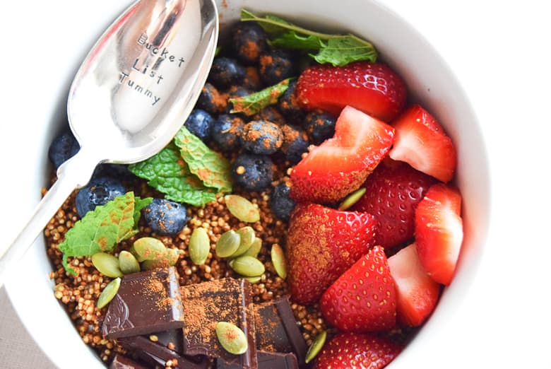 Quinoa breakfast bowl topped with pumpkin seeds and fruit with silver spoon showing