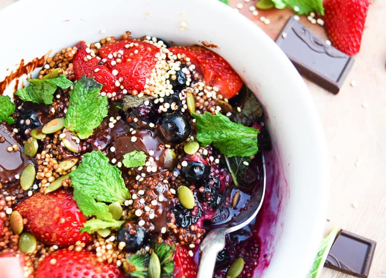 Quinoa breakfast bowl in white bowl with berries and chocolate