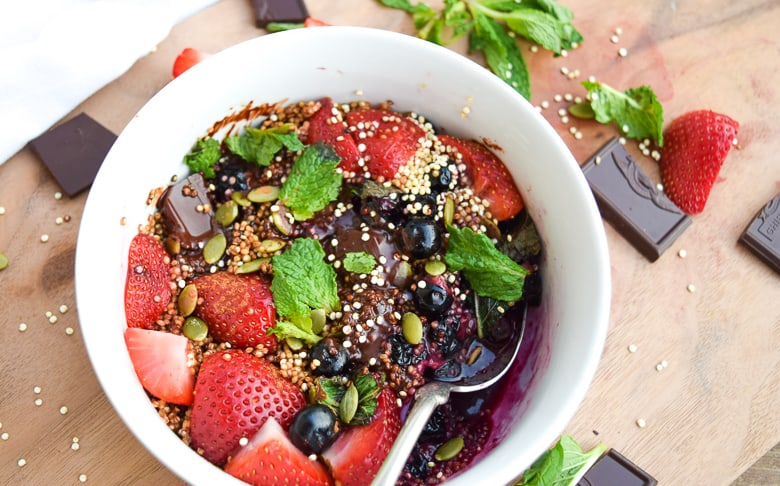 white bowl with toasted quinoa, chocolate, strawberries, blueberries and mint