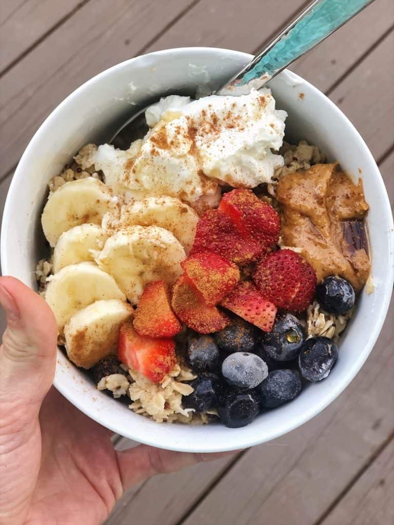 Oatmeal topped with berries, yogurt, peanut butter in white bowl