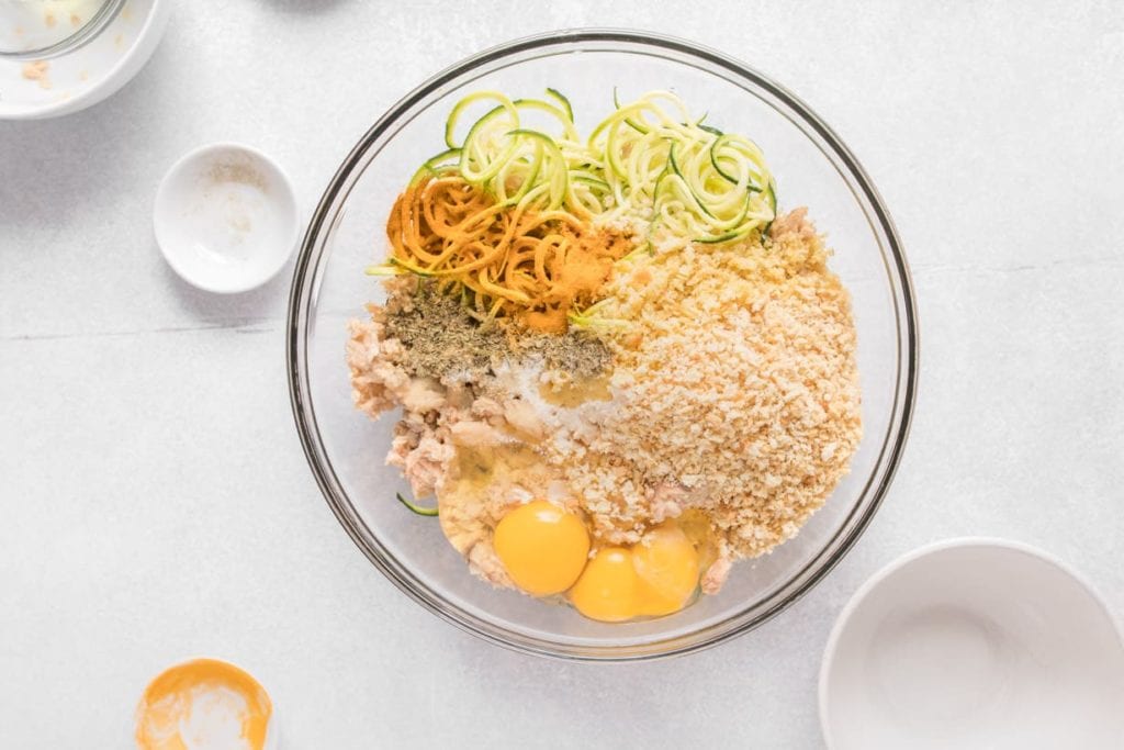 clear bowl with canned salmon, zucchini, eggs and breadcrumbs before mixing and forming into salmon and zucchini fritters