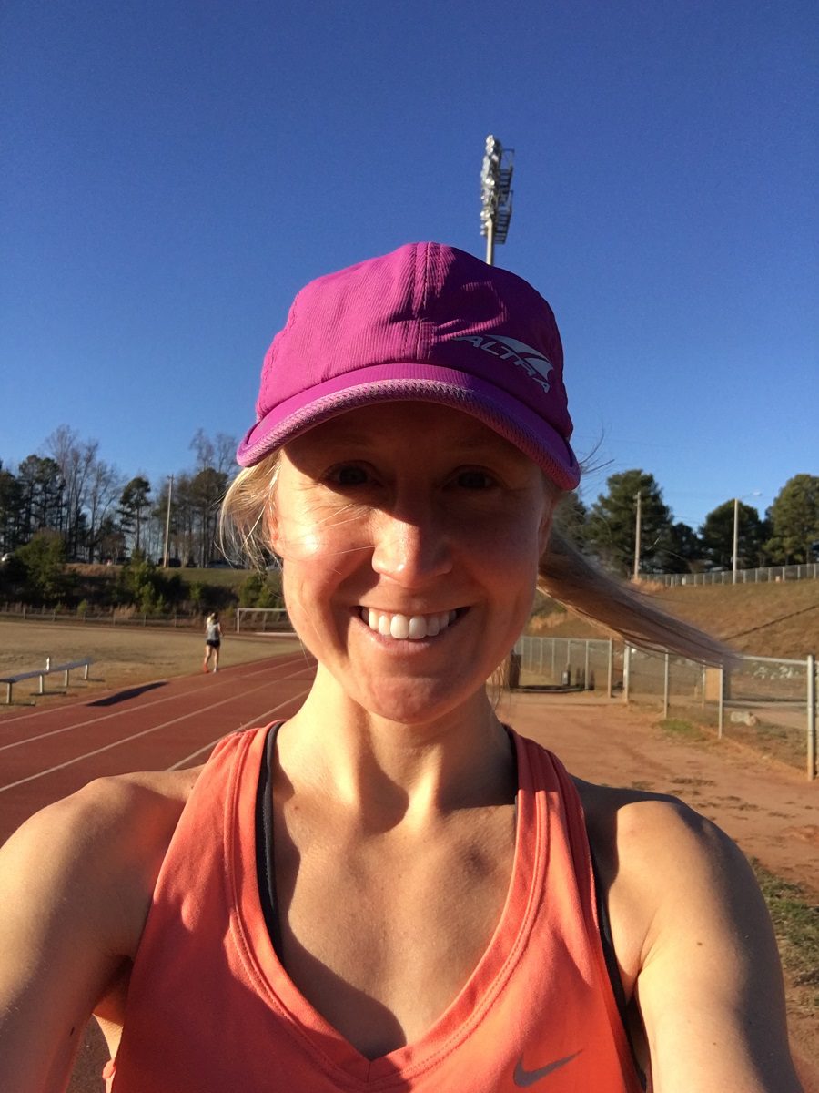 girl in orange tank top and purple hat smiling before doing a workout on the track