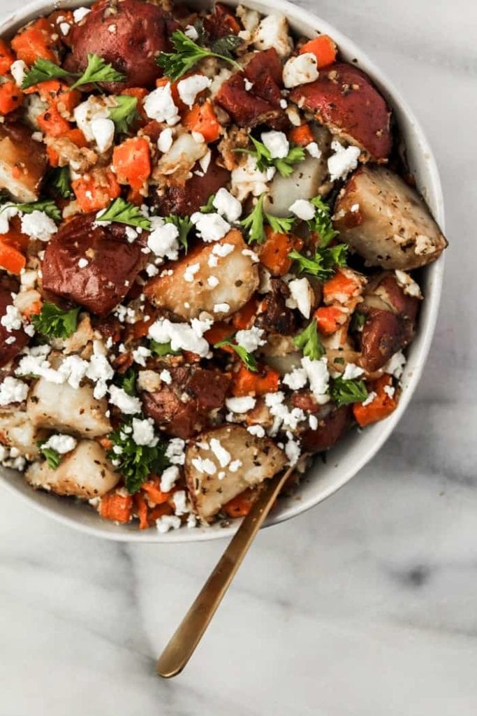 Closeup of slow cooker roasted potatoes and carrots in serving bowl topped with feta cheese and parsley | Bucket List Tummy