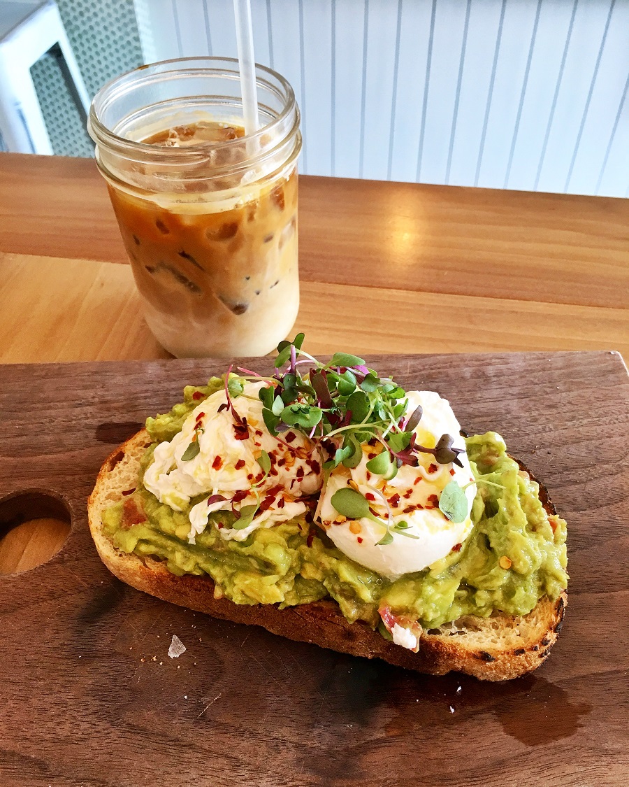Thick avocado toast with iced coffee on wooden table in restaurant