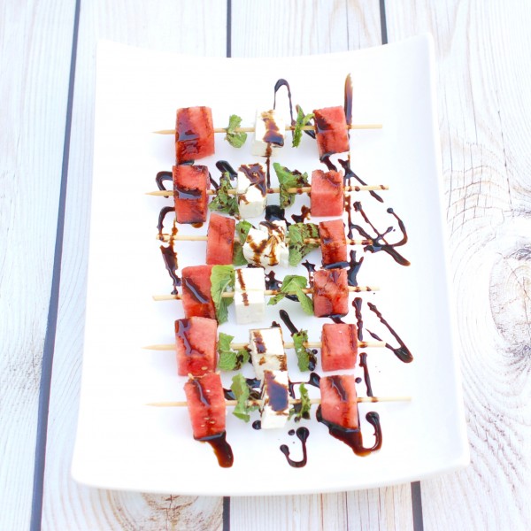 watermelon, cheese and herbs on wooden skewers on white plate with balsamic drizzle