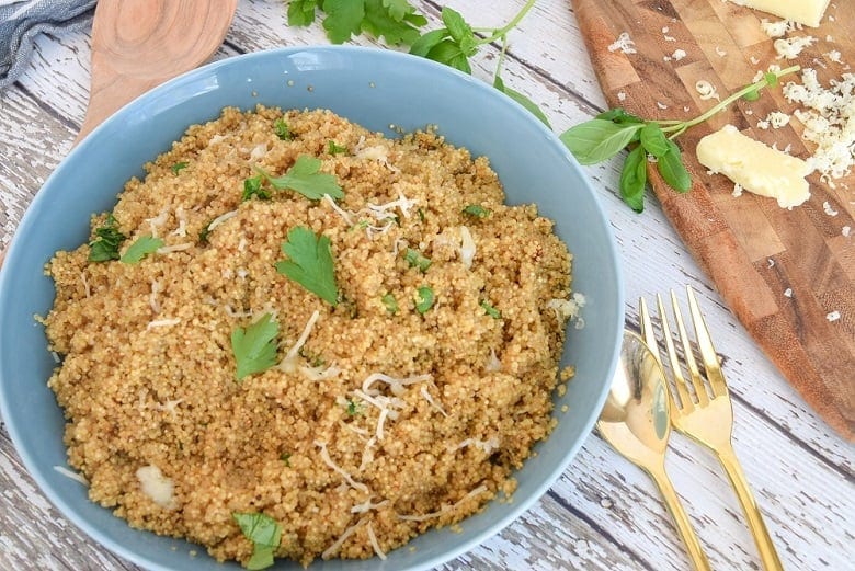 Lemon quinoa recipe in blue bowl topped with shredded cheese and herbs