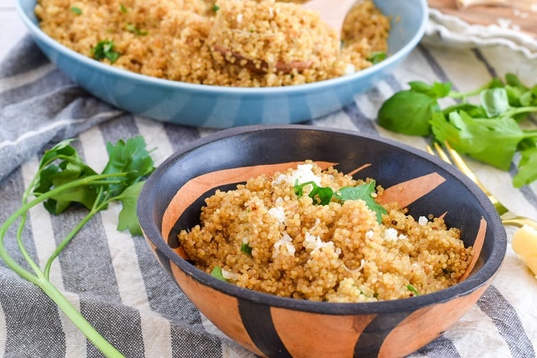 Serving bowl of cheesy quinoa surrounded by fresh herbs