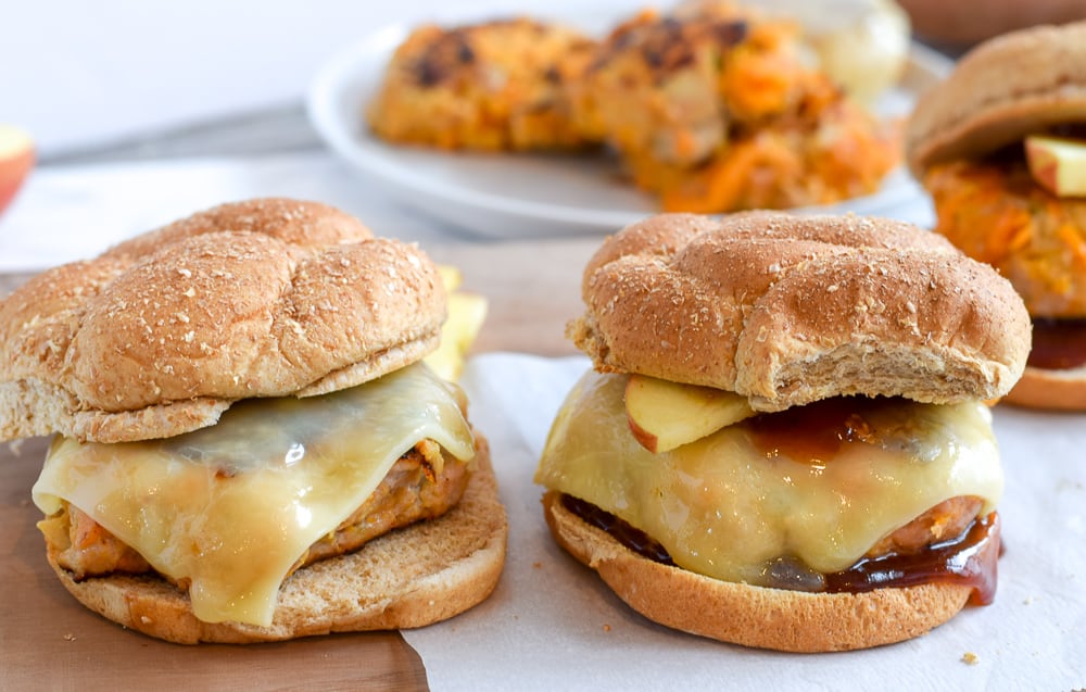 two apple cheddar turkey burgers with apple and cheese and buns on white plate
