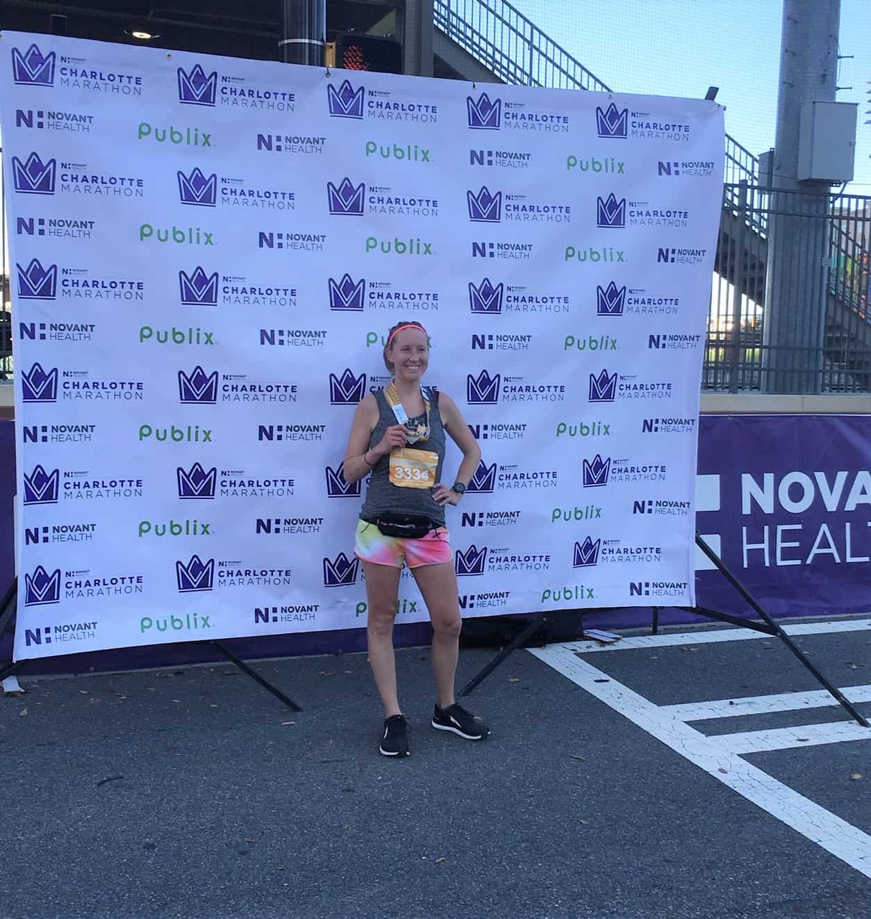 girl holding medal in front of Charlotte Novant Half Marathon screen