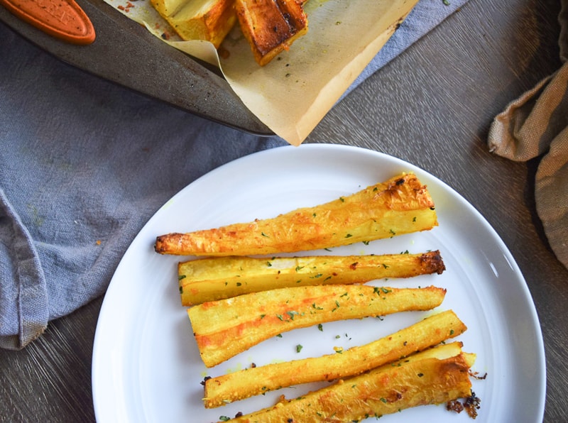 Roasted parsnip fries on a plate seasoned with garlic and turmeric next to baking sheet | Bucket List Tummy