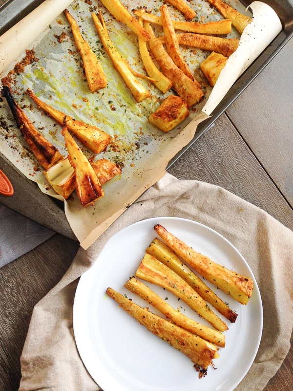 Roasted parsnip fries on a plate seasoned with garlic and turmeric next to baking sheet | Bucket List Tummy
