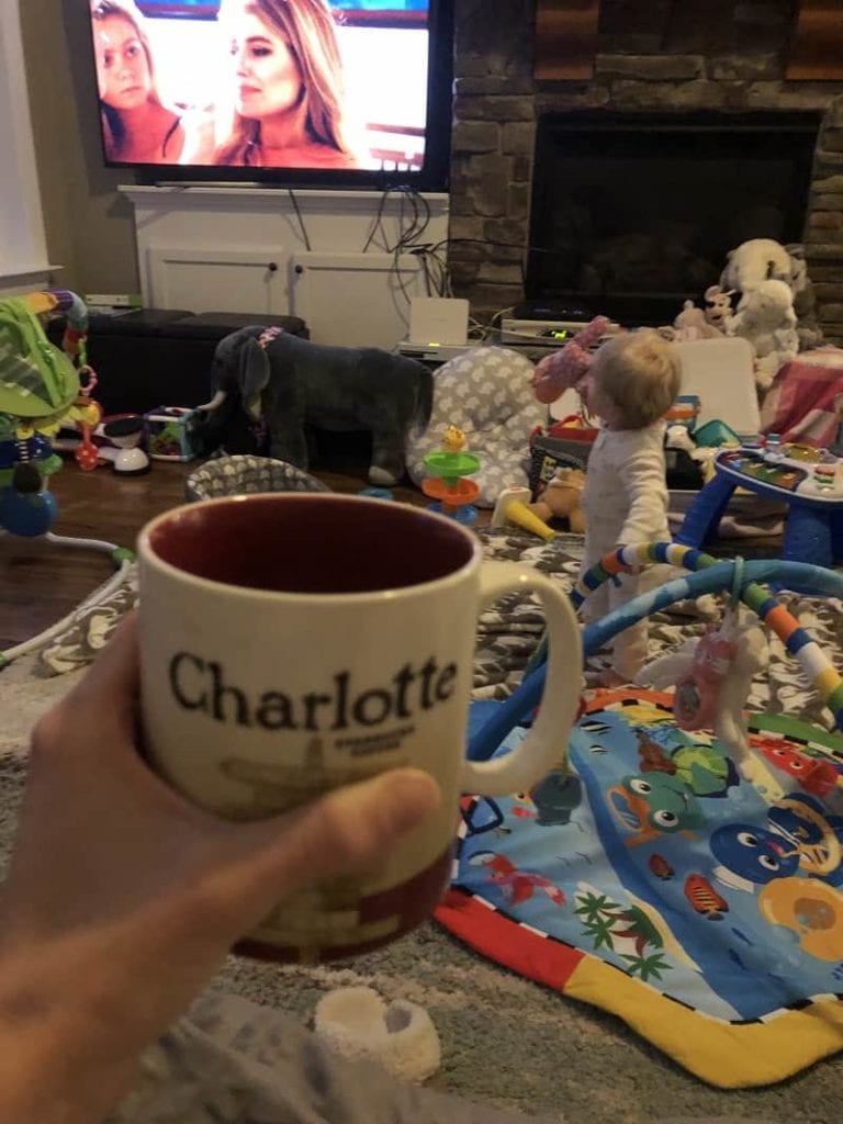 drinking coffee in a room surrounded by baby toys