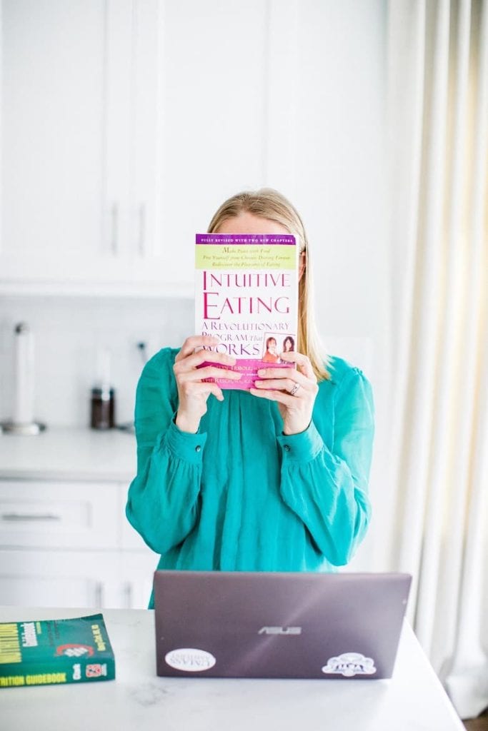 blonde Registered Dietitian holding up Intuitive Eating book