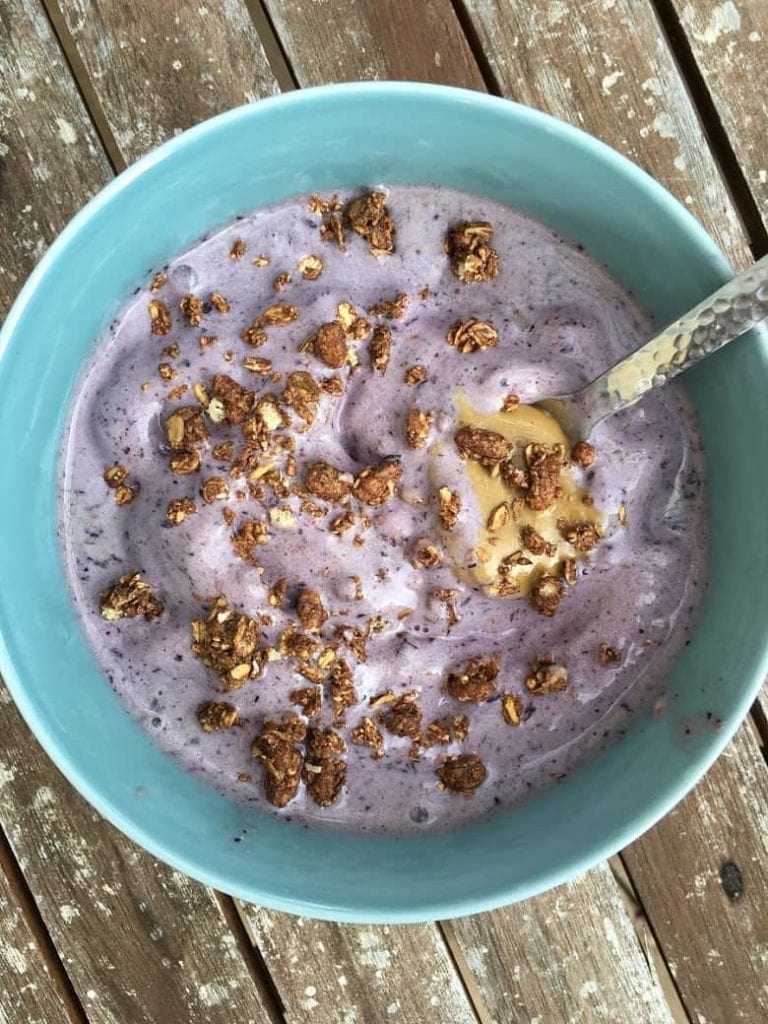 Purple smoothie bowl with granola and spoonful of peanut butter