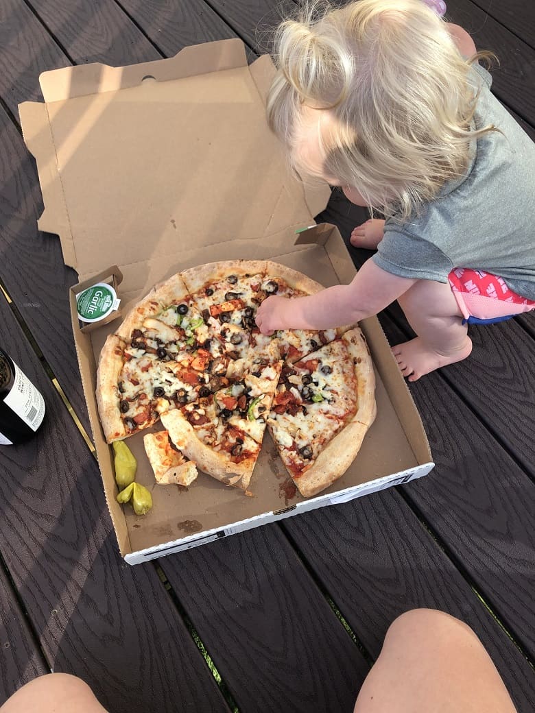 toddler picking toppings off of pizza on outside deck