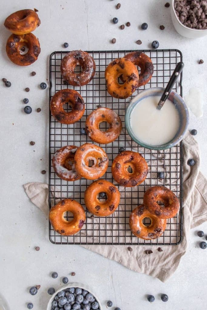 Whole Wheat Donuts with cblueberries and hocolate chips on cooling rack with bowl of icing