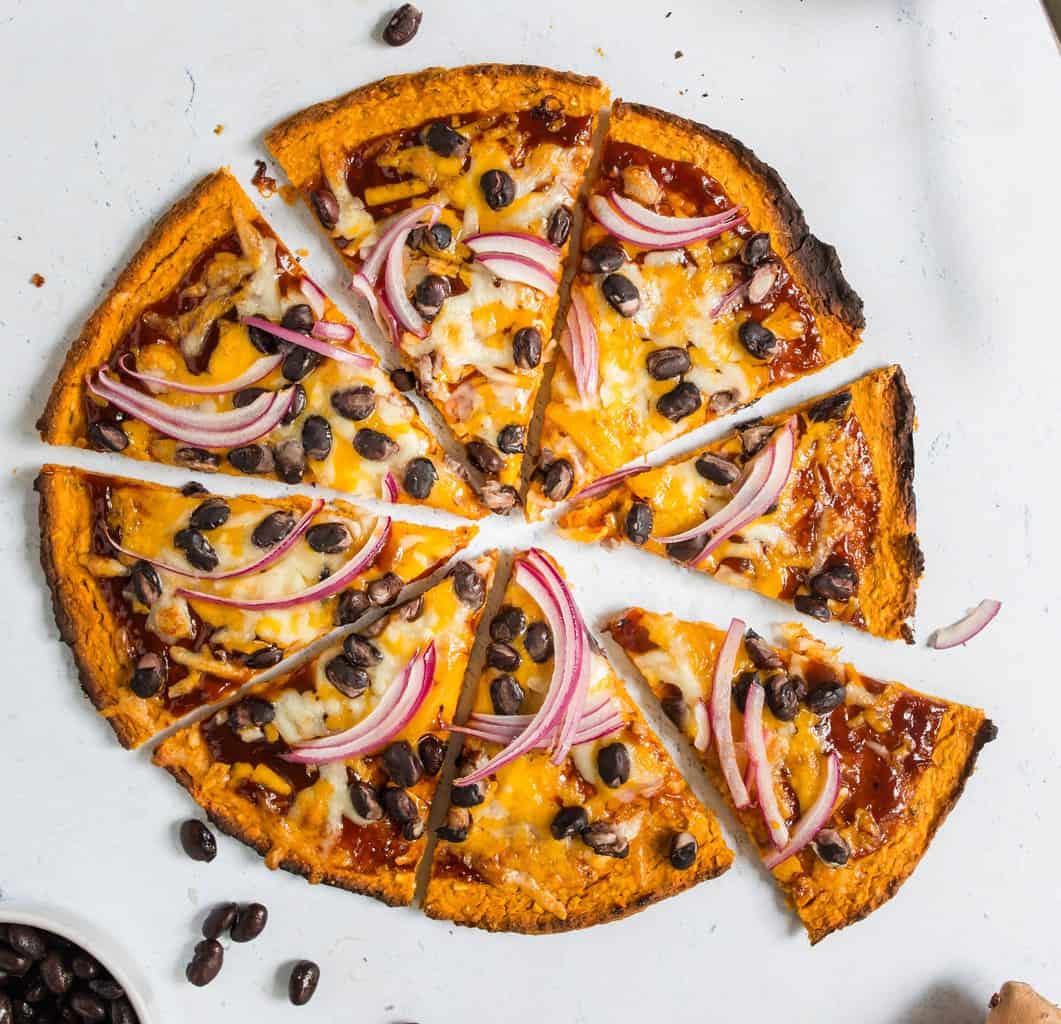 Overhead view of gluten free sweet potato pizza crust topped with black beans and onion 