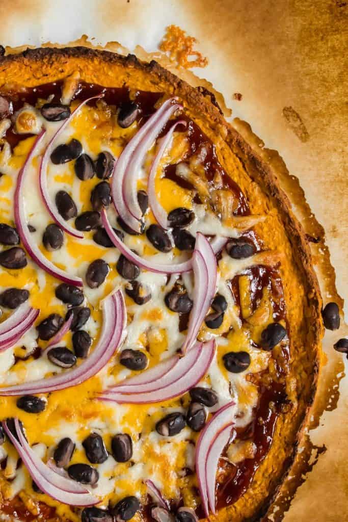 Close up of sweet potato pizza dough topped with onions, black beans and cheese