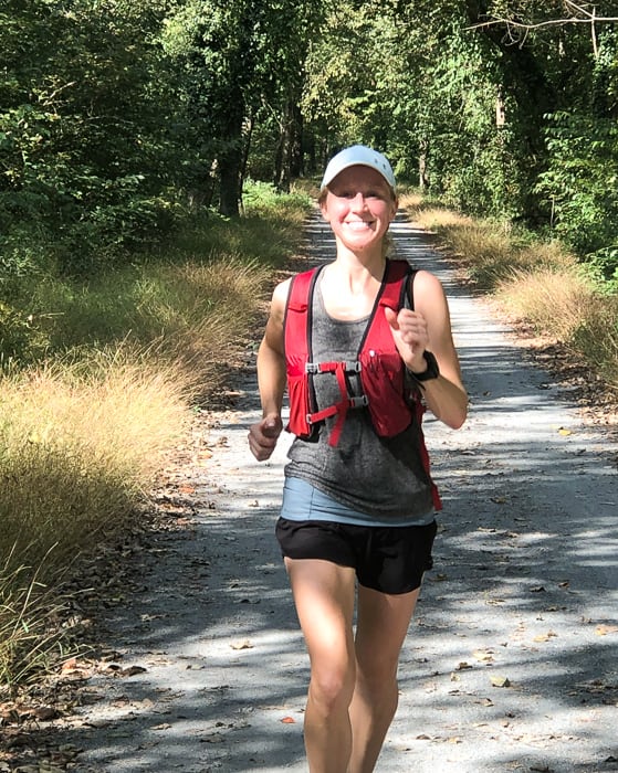 Girl smiling on a trail wearing a running vest