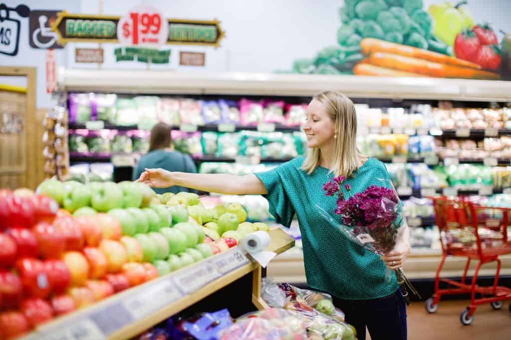 Girl in grocery store looking at produce and holding purple flowers