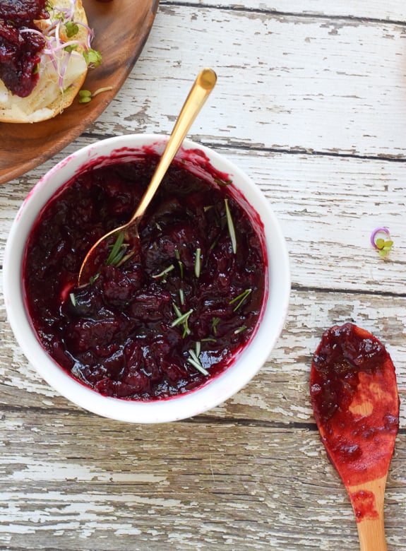 Homemade cranberry sauce in white bowl topped with rosemary