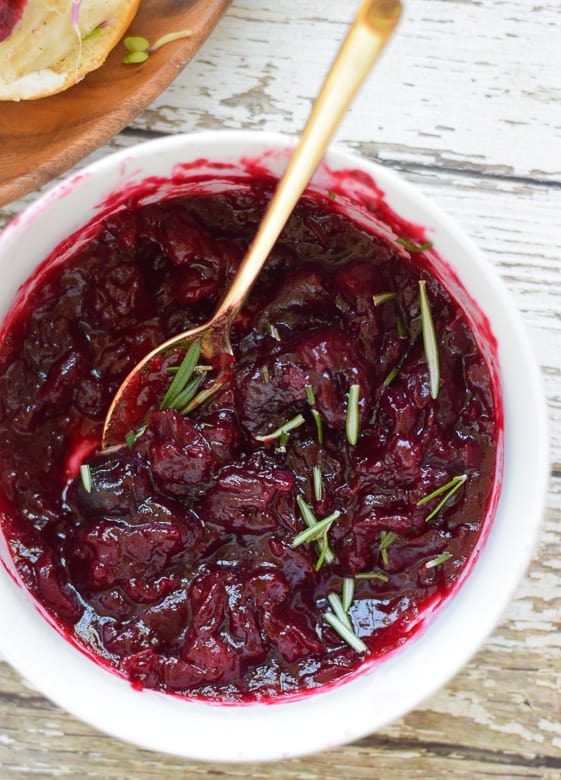 Homemade cranberry sauce in white bowl topped with rosemary