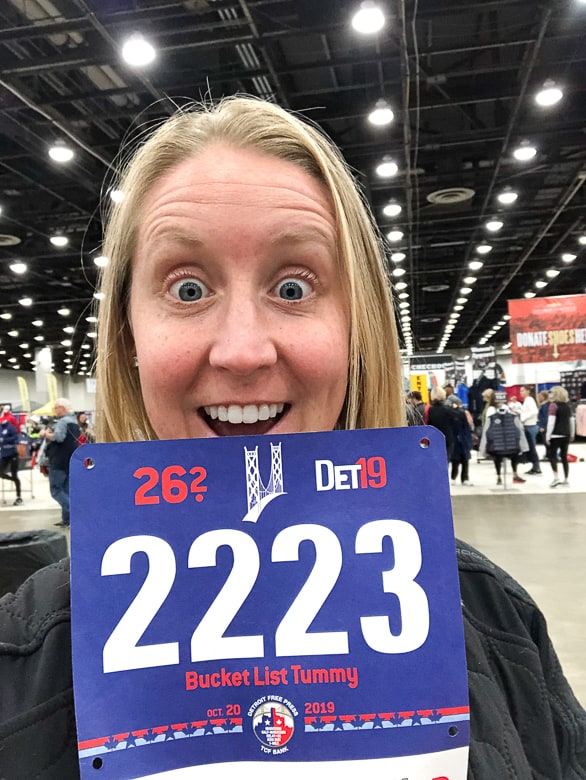 girl holding Detroit Marathon bib for 2019