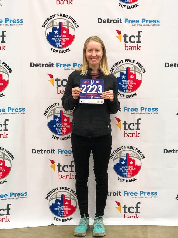 girl holding Detroit Marathon bib in front of background