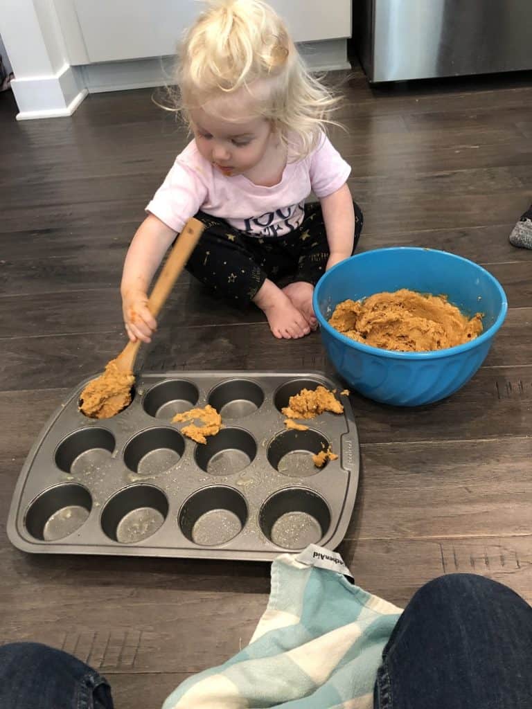toddler spooning batter into muffin tin 