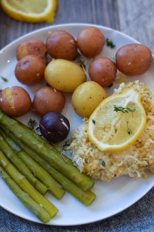 Coconut crusted fish with asparagus and baby potatoes on white plate
