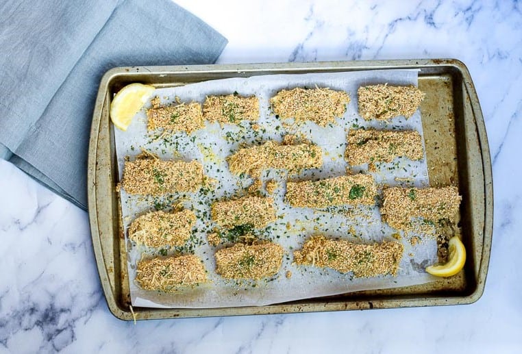 Gluten free fish fingers on baking sheet with herbs and lemon slices