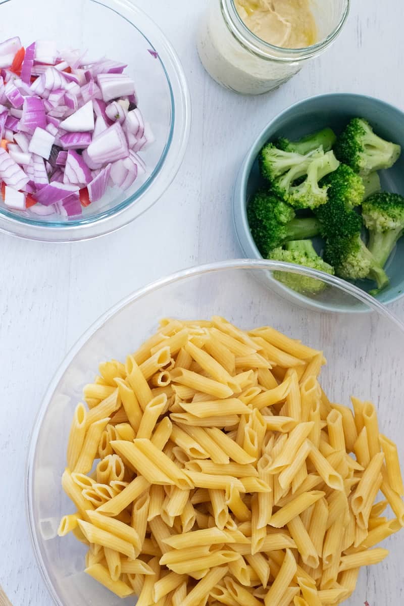 clear bowl with gluten free pasta, bowl of broccoli and bowl of onions and peppers