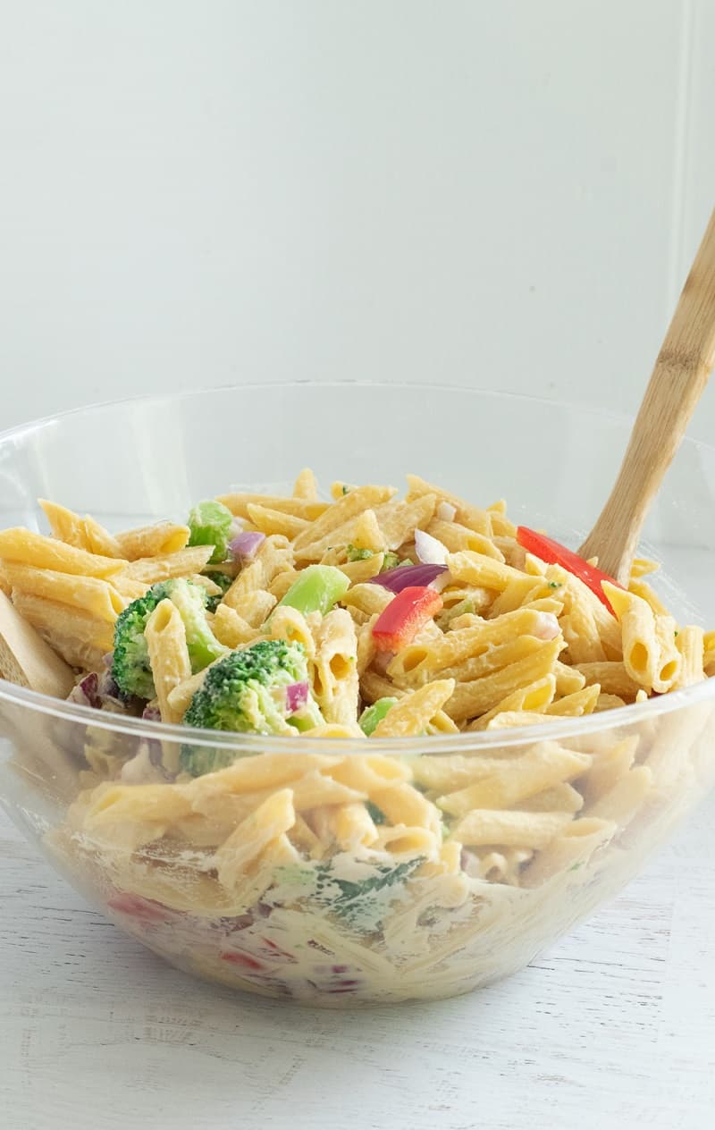 Hummus Pasta Salad in clear mixing bowl with wooden spoon
