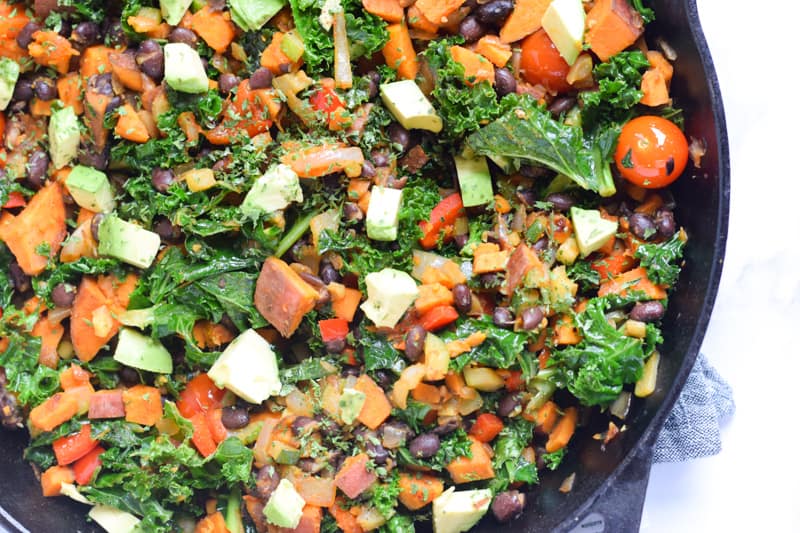 Vegan breakfast hash with kale, tomatoes, beans and sweet potatoes in skillet 