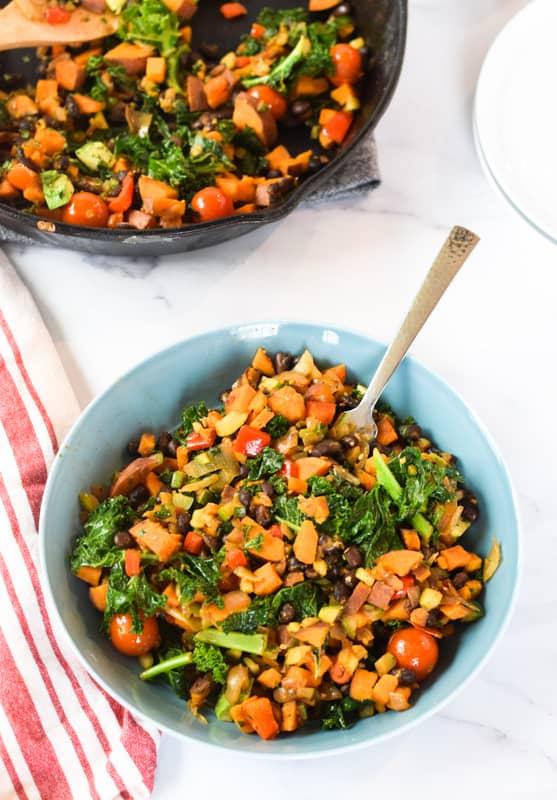 blue plate with sweet potatoes and kale hash on white table with red striped napkin