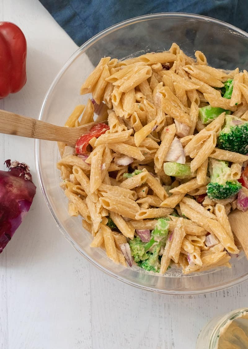 vegan pasta salad in clear bowl with veggies and hummus dressing