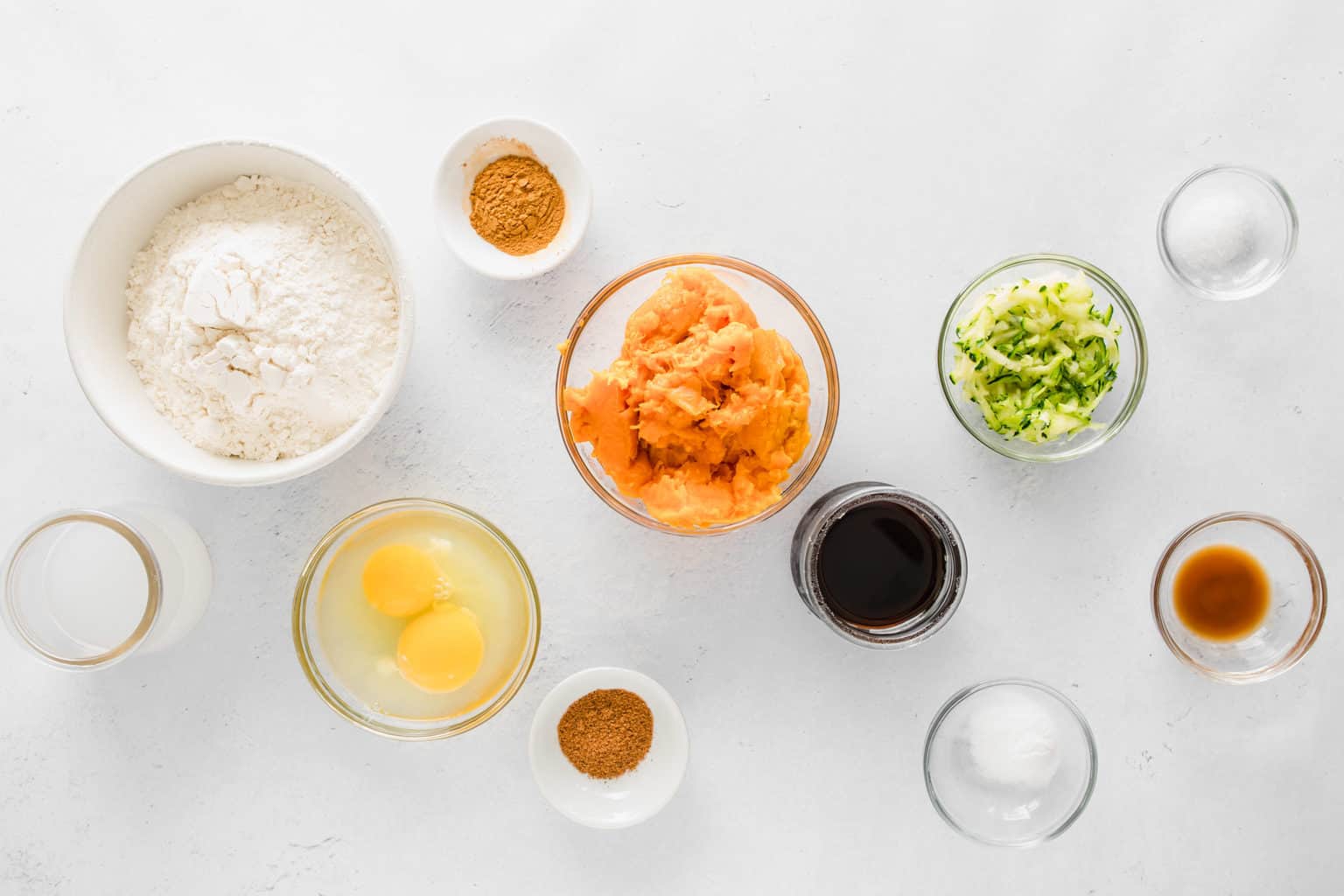 Bowls of ingredients on white countertop to make zucchini sweet potato recipe