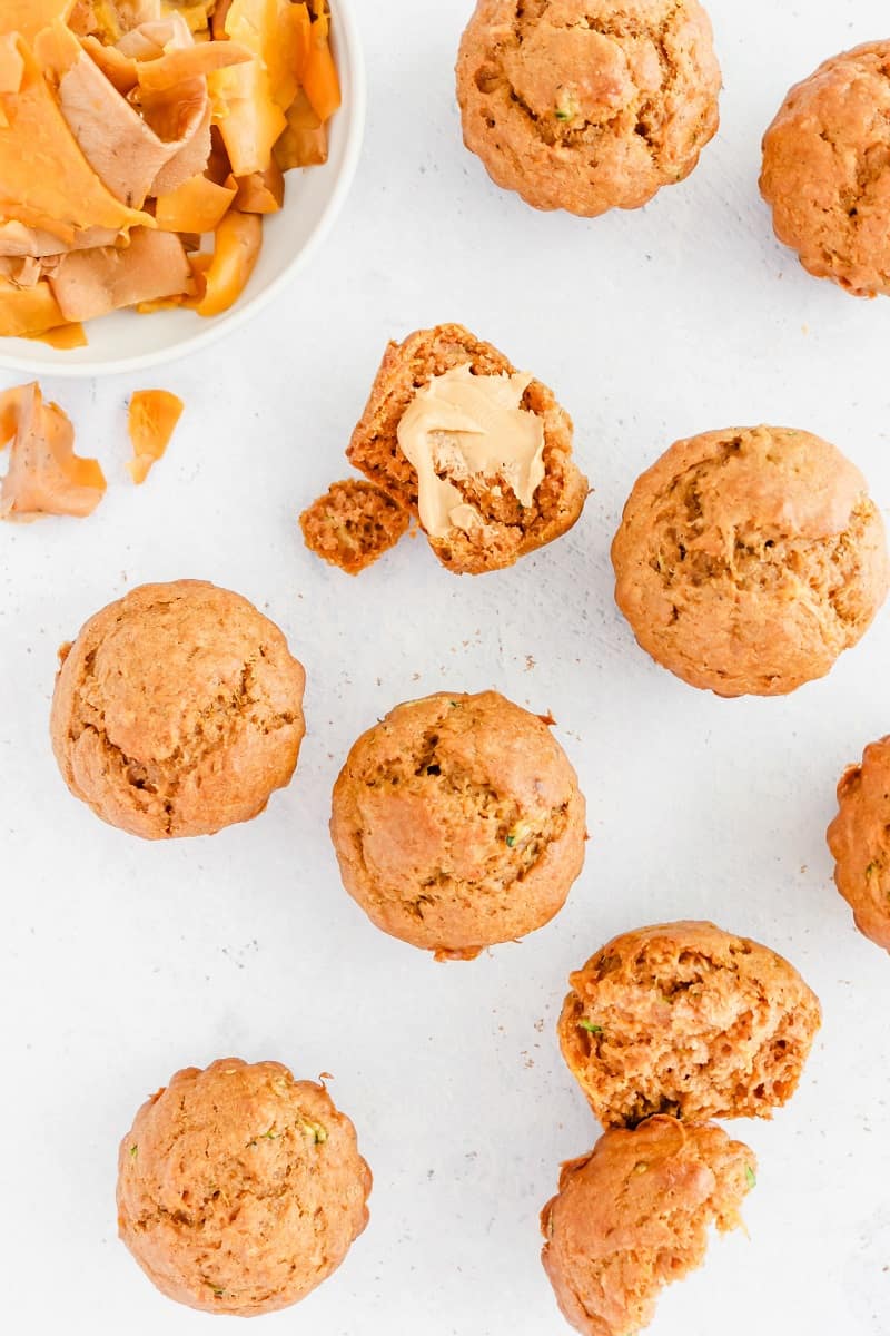 baked zucchini and sweet potato muffins on white countertop with one slathered with peanut butter