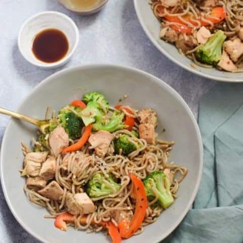 Overhead bowls of egg noodle stir fry with side of soy sauce