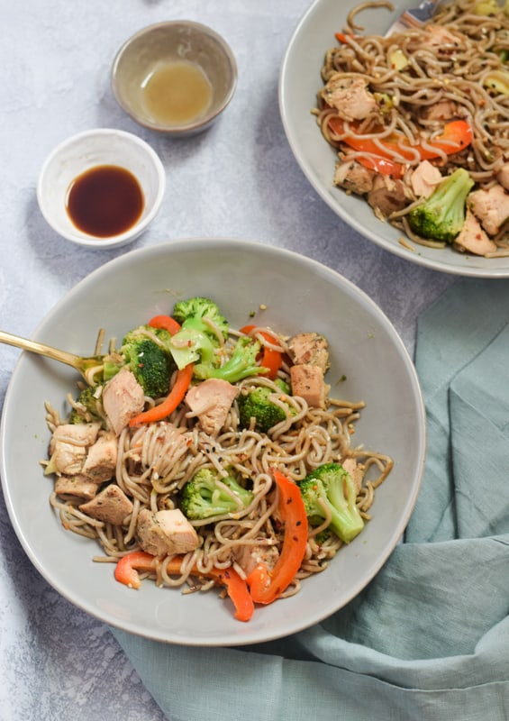 Overhead bowls of egg noodle stir fry with side of soy sauce