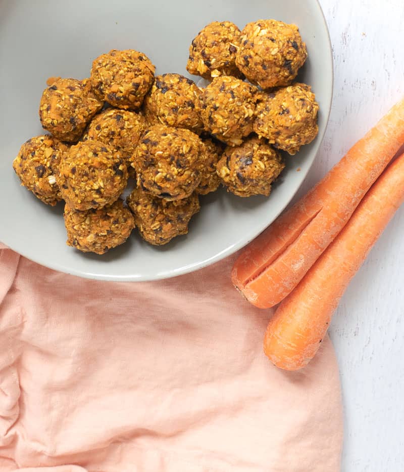 raw carrot cake balls in gray bowl next to carrots